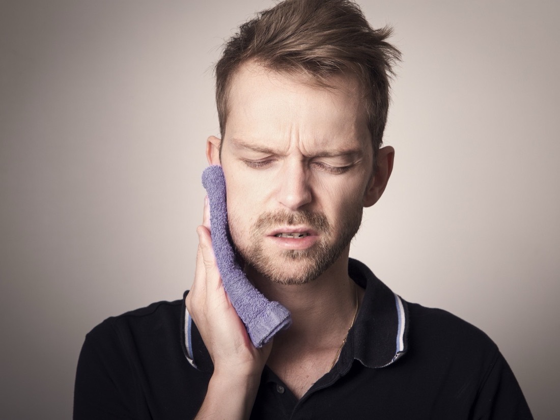 A man holding a cold compress against his jaw from tooth pain